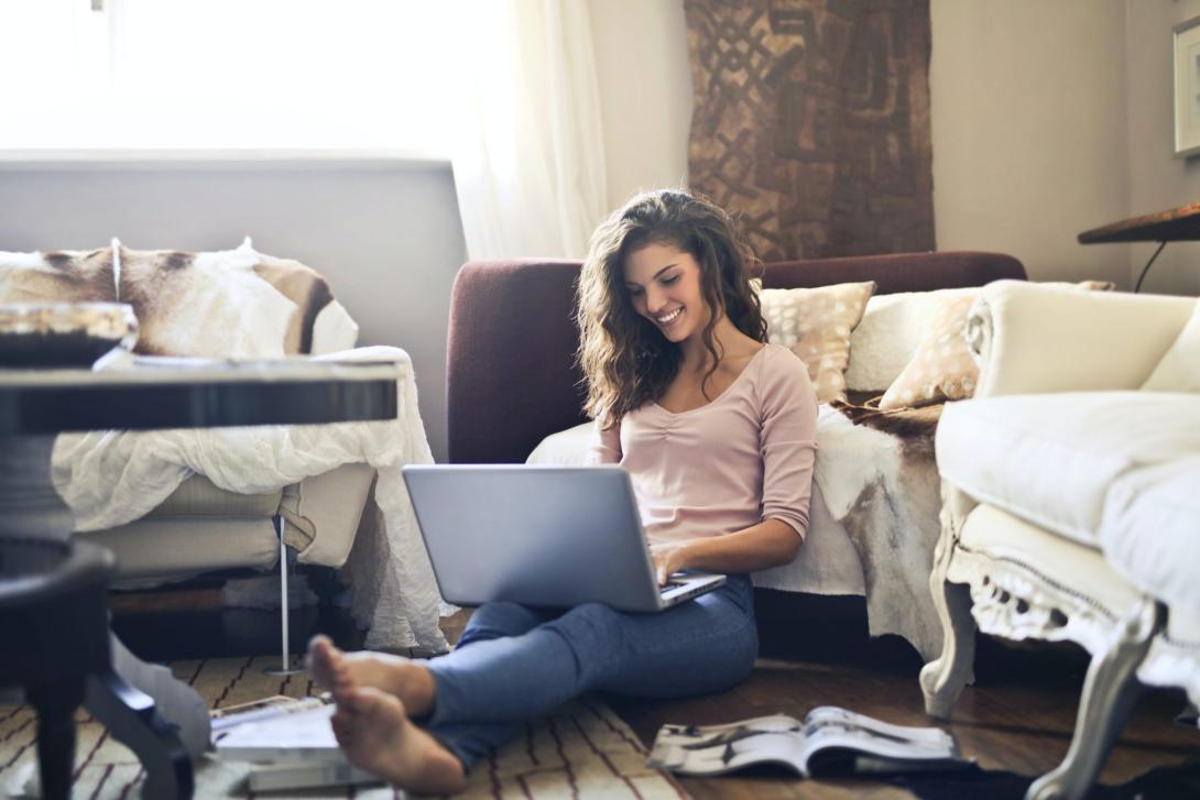 woman sitting on the floor smiling and working on a laptop